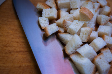Golden brown croutons, sliced ​​bread and knife on wooden surface, create a delicious texture and crunch. Perfect close-up of bread cubes for cooking, recipes or food background