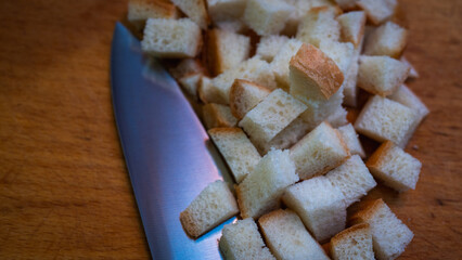 Golden brown croutons, sliced bread and knife on wooden surface, create a delicious texture and crunch. Perfect close-up of bread cubes for cooking, recipes or food background