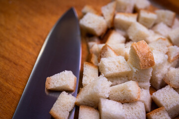 Golden brown croutons, sliced ​​bread and knife on wooden surface, create a delicious texture and crunch. Perfect close-up of bread cubes for cooking, recipes or food background