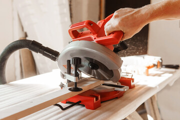 Circular saw in action as a carpenter skillfully cuts wooden planks. Hands hold the wood against...