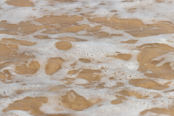 A sandy beach with a foamy, white wave crashing onto the shore