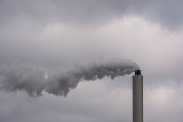 Long trail of smoke from chimney against pale sky. Air quality, industrial activity and environmental degradation illustrated with minimal framing.