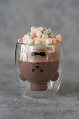 Hot cocoa with marshmallows in a funny glass cup on a gray background. 