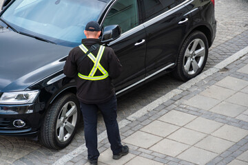A parking enforcement officer in a reflective vest issues a ticket for an illegally parked car on a busy urban street in daylight