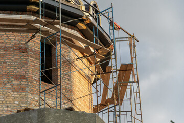 Workers are engaged in construction activities on a historic building, utilizing scaffolding and wooden planks to access the upper sections of the structure