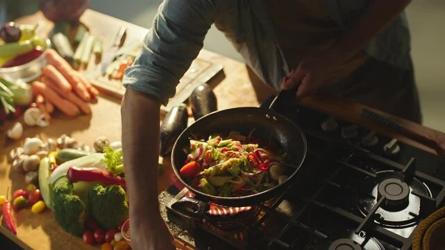 Unrecognizable male chef adding ingredients in vegetable pan. Man sprinkling salt and spices, pouring oil with the vegetables