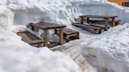Wooden picnic benches surrounded by deep snow on a sunny day at a ski resort