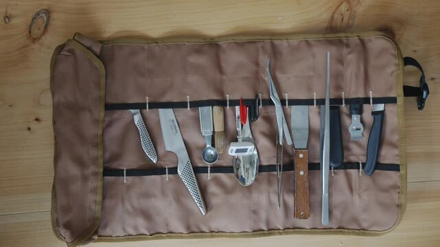 A brown cloth with a bunch of knives and other utensils on it. The knives are of different sizes and shapes