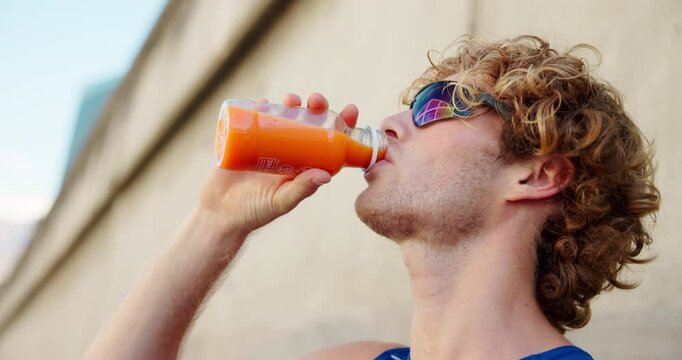 Fitness, man and drink juice in city for wellness, thirsty and healthy beverage for detox. Athlete, sunglasses and carrot extract at wall for antioxidants, vitamin A and energy boost for exercise