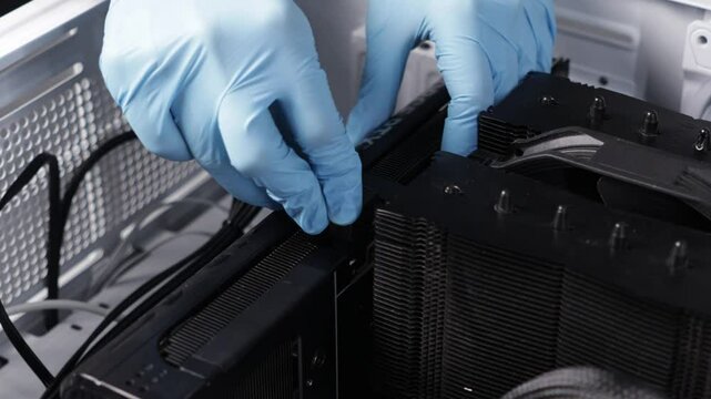 Gloved hands connecting power cable to modern graphics card inside high-end PC case with large CPU air cooler