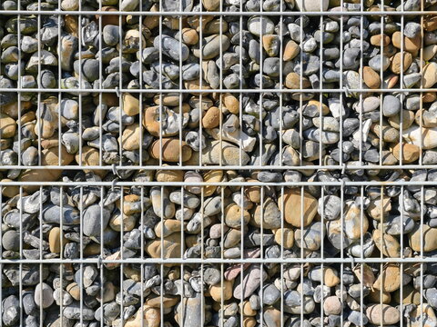 Gabion fence filled with flintstones, stable and durable. Controversial in design but functional as a visual and noise barrier in modern architecture.