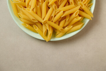 Delicious uncooked penne pasta in a light green bowl ready for cooking