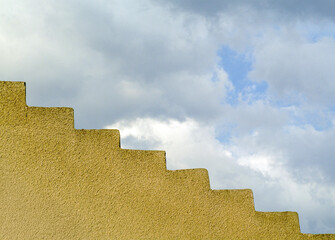 Obraz premium A series of yellow, geometric stairs rise diagonally against a cloudy sky. The contrast between the structured lines of the stairs and the softness of the clouds creates a striking composition.