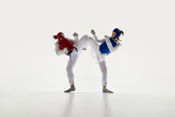 Female taekwondo fighters in red and blue protective gear in motion, fighting with synchronized...