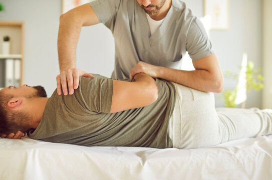 Professional male chiropractor or osteopath specialist works with adult man in manual therapy office. Osteopathic physician help patient with pain relief in upper body using controlled movements.
