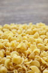 Vertical image showing a pile of uncooked funghetti pasta in sharp foreground with a gradual blur toward the background, emphasizing curly ridged shapes