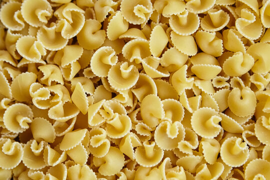 Close-up view of uncooked funghetti pasta showing curled, mushroom-like shapes with ridged edges, forming a textured background in golden yellow tone.