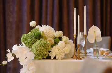 An exquisite arrangement of green and white flowers, complemented by elegant candles, set on a beautifully designed table.