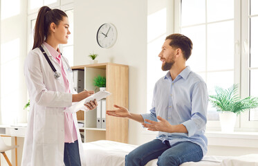 Fototapeta premium Female doctor, consulting male patient in medical office describing symptoms, sharing good lab results, Happy man visit to clinic room, medical care, getting health advice, discussing treatment plan