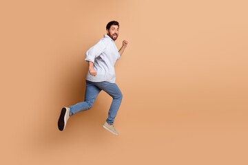 Energetic man in casual outfit jumping mid-air against a beige background capturing lively motion...