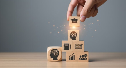 Hand Placing Wooden Blocks with Education Symbols on a Tabletop with a Gray Background