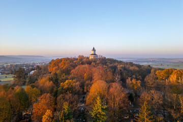 Fototapeta premium The Baroque Humprecht chateau glows softly in the autumn sunrise, surrounded by vibrant foliage above Sobotka in the picturesque Bohemian Paradise of Czechia.