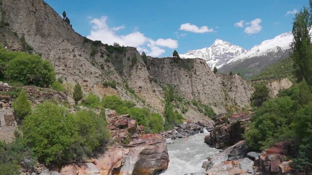 Wide angle scenic shot of River Bhaga flowing in a gorge in front of Snowy Himalayan mountain peaks during the summer season as seen near Keylong in Lahaul and Spiti district, Himachal Pradesh, India.
