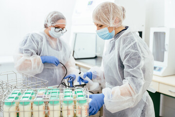 Healthcare workers in sterile gear prepare breast milk bottles for storage using sealing device....