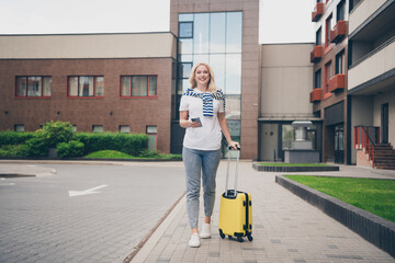 Happy young woman with blond hair enjoying a summer city walk while on vacation, holding a...