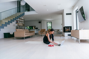 Fototapeta premium Young Beautiful Female Exercising, Stretching and Practising Yoga with Trainer via Video Call Conference in Bright Sunny House. Healthy Lifestyle, Wellbeing and Mindfulness Concept.