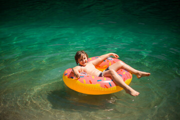 Obraz premium A happy teenager swims and plays in a stunning azure alpine lake. Vibrant, scenic photos capture pure joy and the beauty of nature. Perfect for travel, adventure, and summer themes.