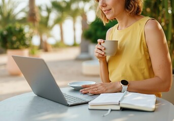 Businesswoman drinking coffee and using laptop at outdoor cafe in tropical resort, combining work and leisure