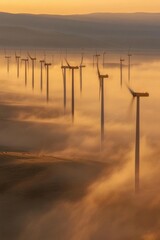 Wind turbines generating power in a foggy and golden sunrise landscape