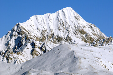 Sharp snow-capped mountains at high altitude against the background of blue sky