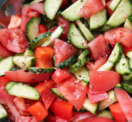 Fresh vegetable salad made of sliced tomatoes, cucumbers, and bell peppers in a deep bowl, sprinkled with ground black pepper. A healthy and colorful dish, perfect for a balanced diet, vegetarian meal