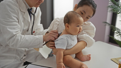 Mother holding baby boy while doctor examines him with stethoscope in hospital clinic, showcasing family love and care in an indoor healthcare setting.