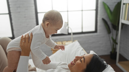 Obraz premium Woman and baby smiling together on bed in cozy bedroom, embodying love and family bond in a bright home environment.