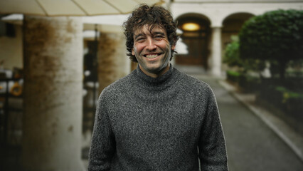 Young man smiling outdoors on a city street, showcasing an attractive and happy expression with a blurred urban background and natural light.