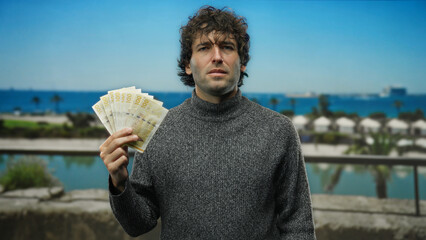 Man holding norwegian banknotes on a seaside beach with blue sky and palm trees background.