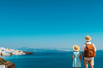 Exploring beautiful coastal view, man and girl in summer hats admire stunning landscape of Santorini, Greece, with its iconic blue waters and colorful buildings