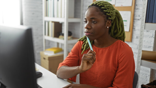 Woman in braids sitting at a desk in an office with bookshelves in the background, focused on work in an indoor setting, embodying professional and modern workplace aesthetics. - Powered by Adobe