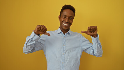Young black man smiling confidently, pointing thumbs at himself against a vibrant yellow background...