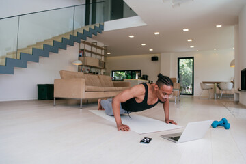Training At Home. Sporty african american man doing the training while watching an online tutorial...