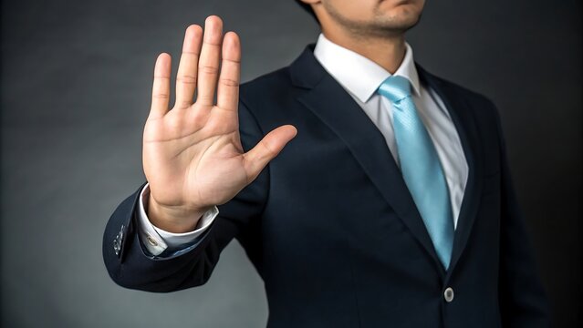 A businessman in a suit raising his hand in a stop gesture against a dark gray background image view