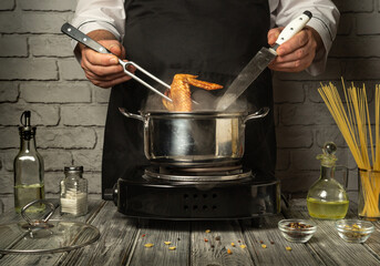 In a modern kitchen, a chef skillfully uses a fork and knife to handle the chicken legs cooking in a pan. The warm atmosphere is illuminated by the stove