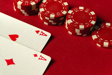 Two aces lay facing up on a red felt table surrounded by stacks of red poker chips. The atmosphere...