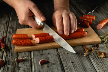 Hands expertly slice smoked sausage on a wooden board surrounded by fresh herbs and spices,...