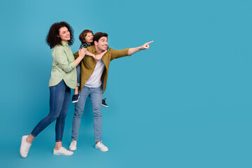 Obraz premium Young happy family enjoying quality time posing together against blue background, pointing towards something with cheerful expressions