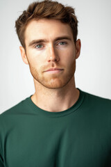 Fototapeta premium The image is a tight, close-up studio shot of a young Caucasian man's face and upper chest. The man has short reddish-brown hair and a light reddish beard and stubble. His expression is neutral,