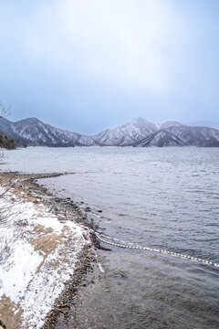 Lake Chuzenji, on the mountains in Nikko, Japan, during winter season with snow fall under cloudy sky and very cold weather. Japanese letters were name of public gate in Japanese faith.